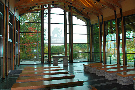 A kneeling Marine at prayer with the words of the Marine Prayer is etched on the wall behind the altar inside the Chapel, just outside the front gate of MCB Quantico, VA. From its granite floor to the 16 pews constructed of stacked fieldstone with granite bench tops to the plain stone altar and natural cedar ceiling beams, the interior is dignified and calming, befitting a house of worship.