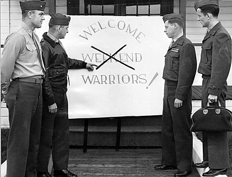 Standing outside the PA shop at NAS Quincy, MA the morning of reporting for duty. Don Knight is on the far right. He is carrying his toothbrush and comb (I had a lot of  good teeth and hair in those days) and standing on a curb facing the duty officer which makes his 5’7” look like 5’11”.   A big sign nearby reads: “Welcome Weekend Warriors.”  The word Weekend has been  covered with a big X.  