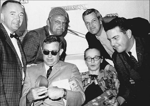 Marine Combat Correspondents gather at the bedside of Dickey Chapelle, recovering from a parachuting accident in a New York hospital, in 1964. (L-R) Maj. Bob “Mo” Morrisey, Lou Lowery, Dick Phelan, Steve Stibbens, and Ron Lyons seated with Dickie. Lowery, Lyons and Stibbens were were all members of the Leatherneck Magazine staff. The following year, Chapelle went to Vietnam to be with her beloved Marines in combat. 