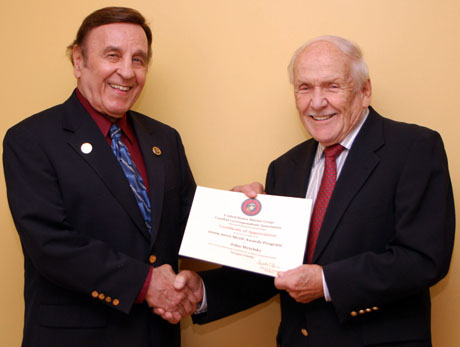 "JOB WELL DONE ," says USMCCCA member Don Knight (r) as he shows off the Certificate of Appreciation delivered to John Metelsky of Silver Spring, MD. Certificates were forwarded to judges who reviewed entries in this year's USMCCCA Merit Awards competition. Metelsky, completing his second stint as a photo judge, is a former information chief for the U.S. Agency for International Development and an editor/photographer for the National Press Club. (Photo by Sonia Metelsky).